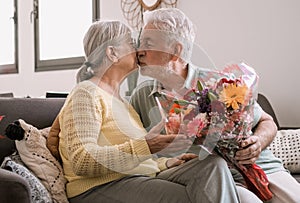 Senior man giving bouquet of flowers at his wife sitting on the sofa at home for anniversary