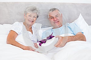 Senior man giving gift to wife in bed