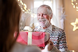 Senior man giving present to unrecognizable woman indoors at home at Christmas.