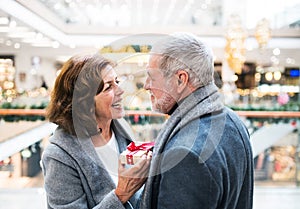 A senior man giving a present to a woman at shopping center at Christmas time.