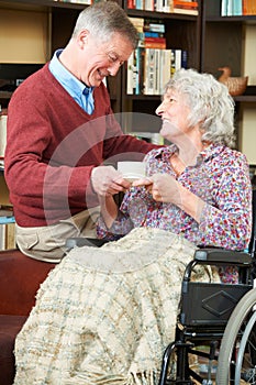 Senior Man Giving Wife In Wheelchair Cup Of Tea