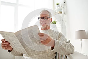 Senior man in glasses reading newspaper at home