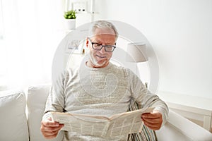 Senior man in glasses reading newspaper at home