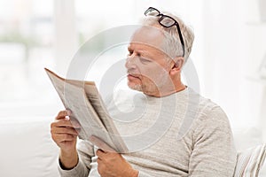 Senior man in glasses reading newspaper at home