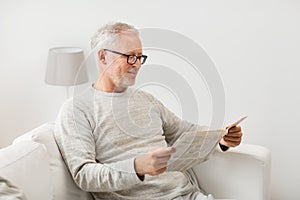 Senior man in glasses reading newspaper at home