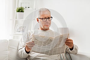 Senior man in glasses reading newspaper at home