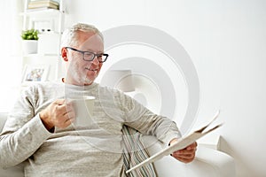 Senior man in glasses reading newspaper at home