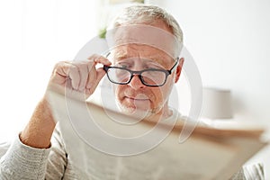 Senior man in glasses reading newspaper at home