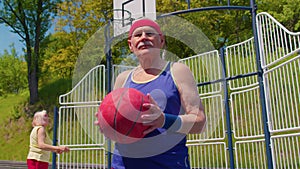 Senior man grandfather athlete posing with ball, looking at camera on playground basketball court