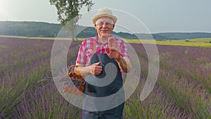 Senior man grandfather farmer growing gardening lavender plant in herb garden, waving hands hello