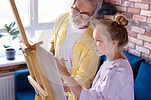 Senior man, grandfather and his granddaughter drawing, painting together