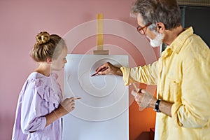 Senior man, grandfather and his granddaughter drawing, painting together