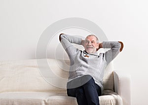 Senior man in gray sweater sitting on sofa, studio shot.
