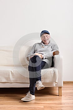 Senior man in gray sweater sitting on sofa, studio shot.