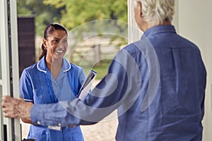 Senior Man Greeting Female Nurse Or Care Worker Making Home Visit In Uniform At Door