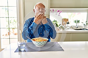 Senior man with grey hair eating pasta spaghetti at home bored yawning tired covering mouth with hand