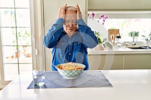 Senior man with grey hair eating pasta spaghetti at home suffering from headache desperate and stressed because pain and migraine