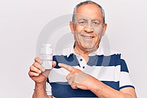 Senior man with grey hair holding bottle of pills smiling happy pointing with hand and finger