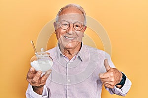 Senior man with grey hair holding bowl with sugar smiling happy and positive, thumb up doing excellent and approval sign