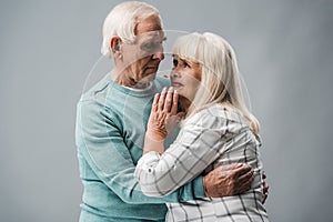 senior man with grey hair hugging upset wife on grey.