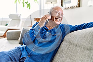 Senior man with grey hair sitting on the sofa at the living room of his house having a conversation speaking on the phone