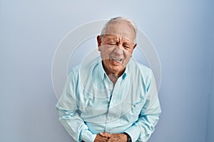 Senior man with grey hair standing over blue background with hand on stomach because indigestion, painful illness feeling unwell