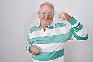 Senior man with grey hair standing over white background strong person showing arm muscle, confident and proud of power