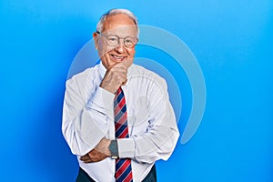 Senior man with grey hair wearing business suit and tie smiling looking confident at the camera with crossed arms and hand on chin