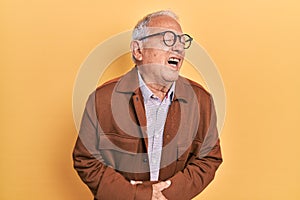 Senior man with grey hair wearing casual jacket and glasses with hand on stomach because nausea, painful disease feeling unwell