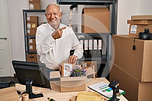 Senior man with grey hair working at small business ecommerce smiling happy pointing with hand and finger to the side