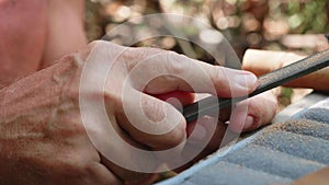 Senior man grinds the cork by file to make a handiwork flute, close-up