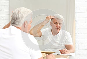 Senior man with hair loss problem looking in mirror