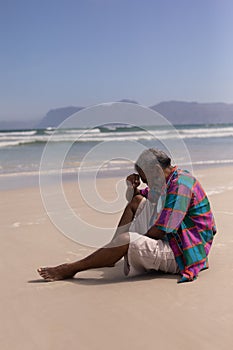 Senior man with hand on forehead sitting on beach