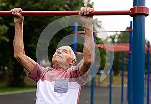 Senior man hanging from pullup bar outoors