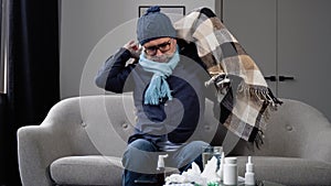 Senior man in a hat suffering from a common cold and flu or allergy sit at home wrapped in blanket while he have a