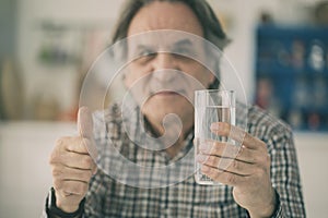 Senior man having glass of water and showing his thumb in kitchen photo