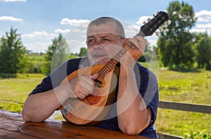 Senior man having rest outdoor playing mandolin