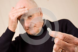 Senior man with headache holding tablet or pill