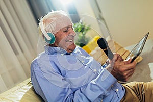 Senior man in headphones singing karaoke, using digital tablet