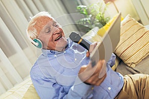 Senior man in headphones singing karaoke, using digital tablet
