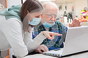 Senior man is helped by his caregiver to using laptop at home during Coronavirus Pandemia photo