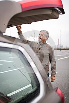 Senior man by his car, closing the trunk lid in a mall parking