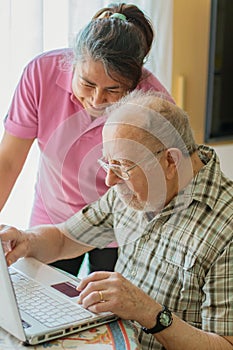 Senior man and his caregiver with laptop at home spending time togheter