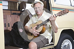 Senior Man With His Dog Playing Guitar In Campervan