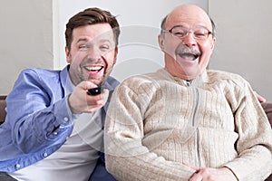 Senior man and his mature son wathcing comedy laughing on funny jokes