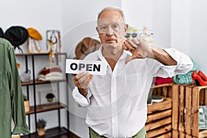 Senior man holding banner with open text at retail shop with angry face, negative sign showing dislike with thumbs down, rejection