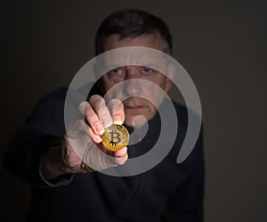 Senior man holding a bitcoin at arms length