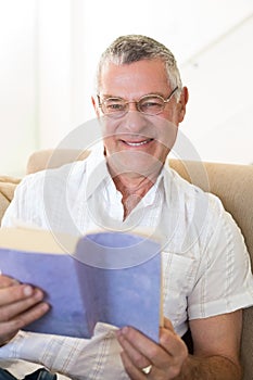 Senior man holding book on sofa