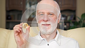 Senior man holding cryptocurrency bitcoin. Shiny virtual money of online trade. Concept of savings