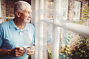 Senior man holding cup and looking out of the window